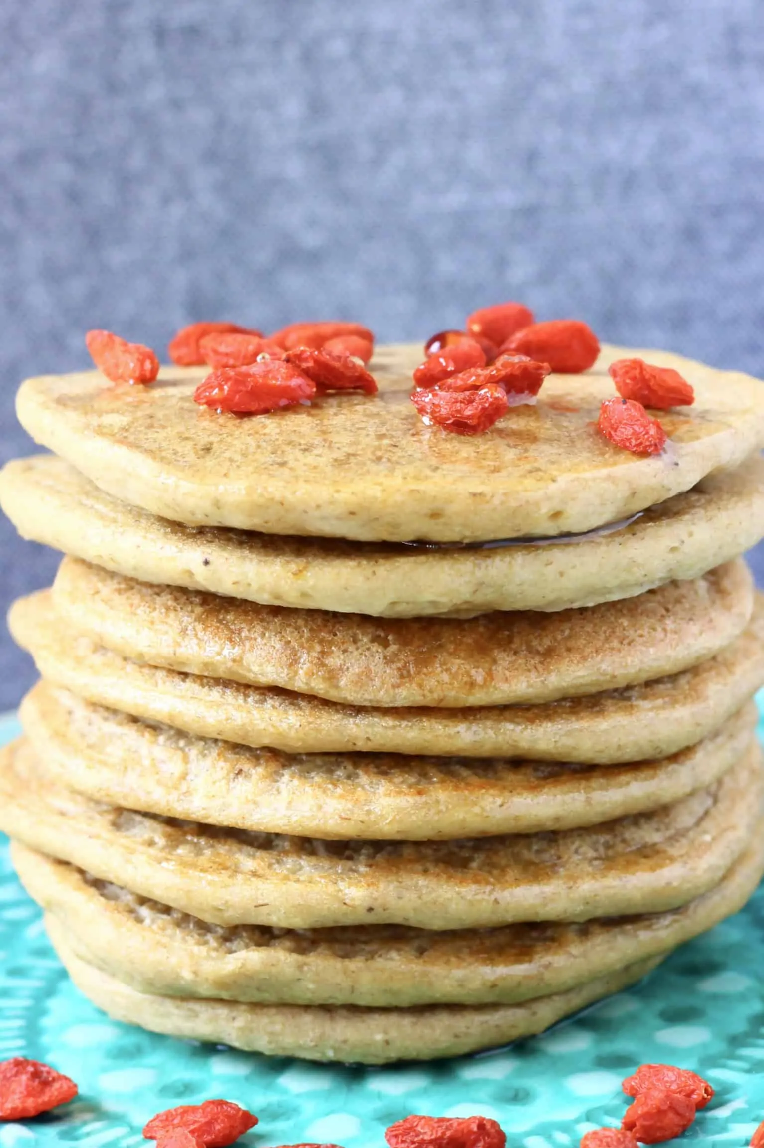 A stack of banana oatmeal pancakes decorated with goji berries on a green plate against a grey background