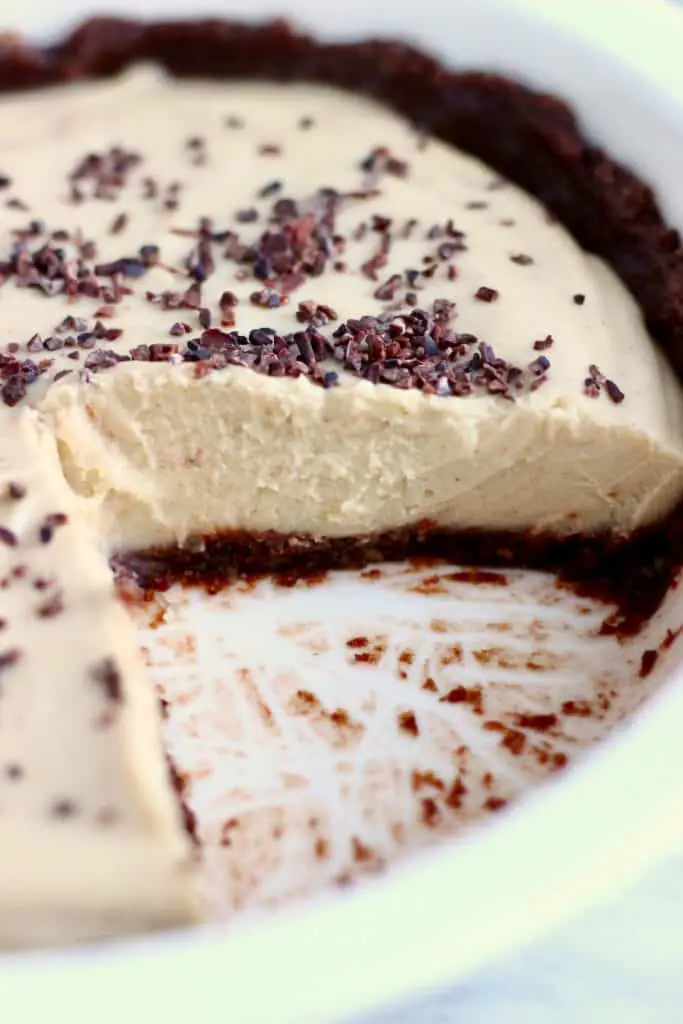 Photo of a sliced pie in a white pie dish - a brown chocolate crust with a light brown filling and sprinkled with cacao nibs