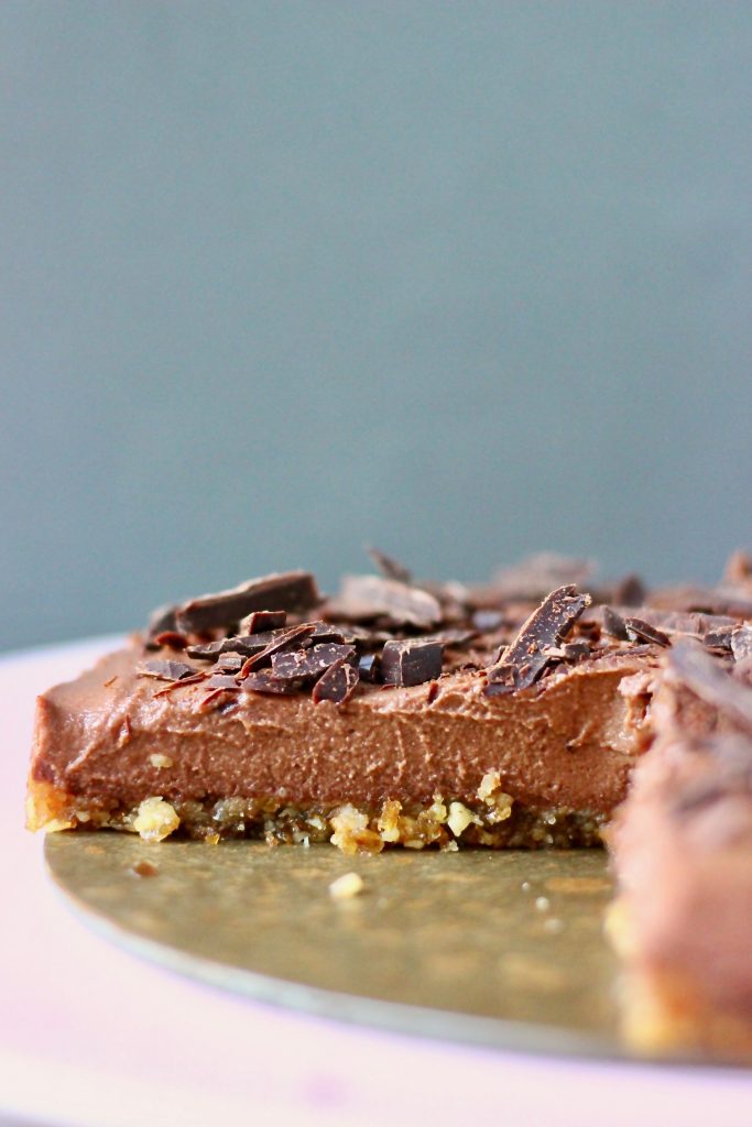 A chocolate cheesecake topped with chocolate shavings on a pink surface against a grey background