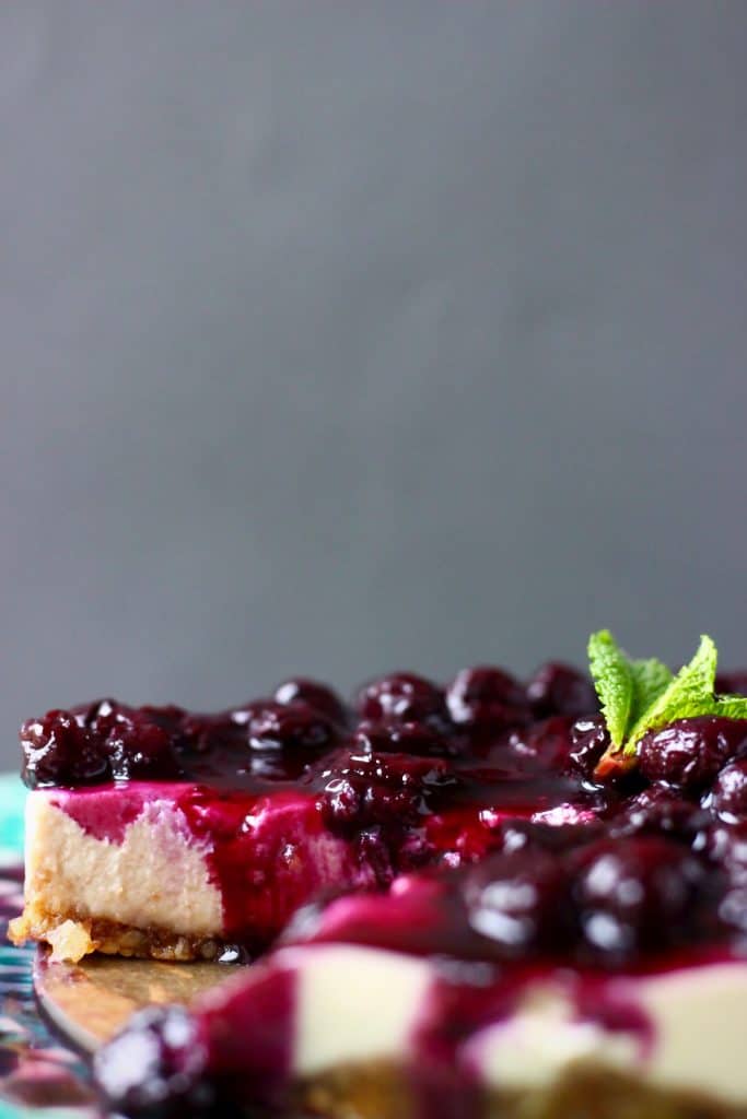 Sliced cheesecake topped with blueberry sauce and a sprig of mint against a grey background