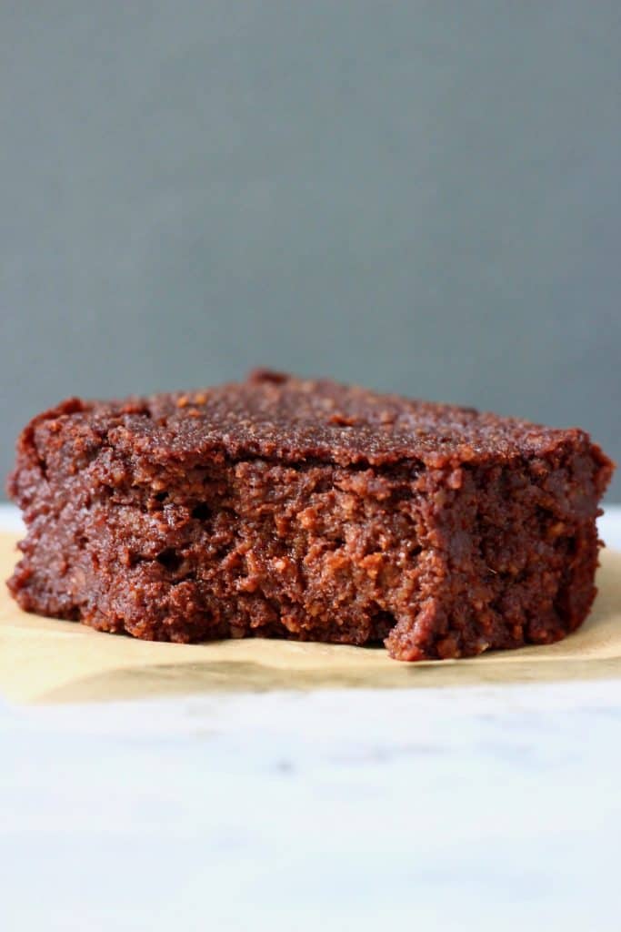 Photo of a chocolate brownie with a bite taken out of it on a piece of brown baking paper against a grey background