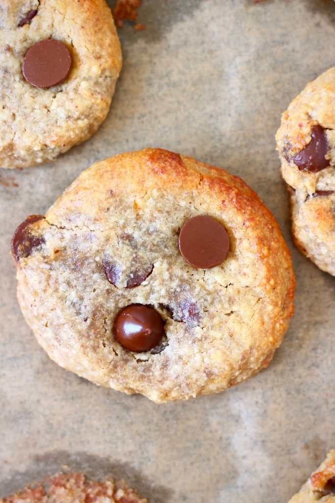 Three chocolate chip cookies on a sheet of brown baking paper