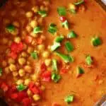 Red curry sauce with chickpeas, red peppers and green peppers in a black pan against a white background
