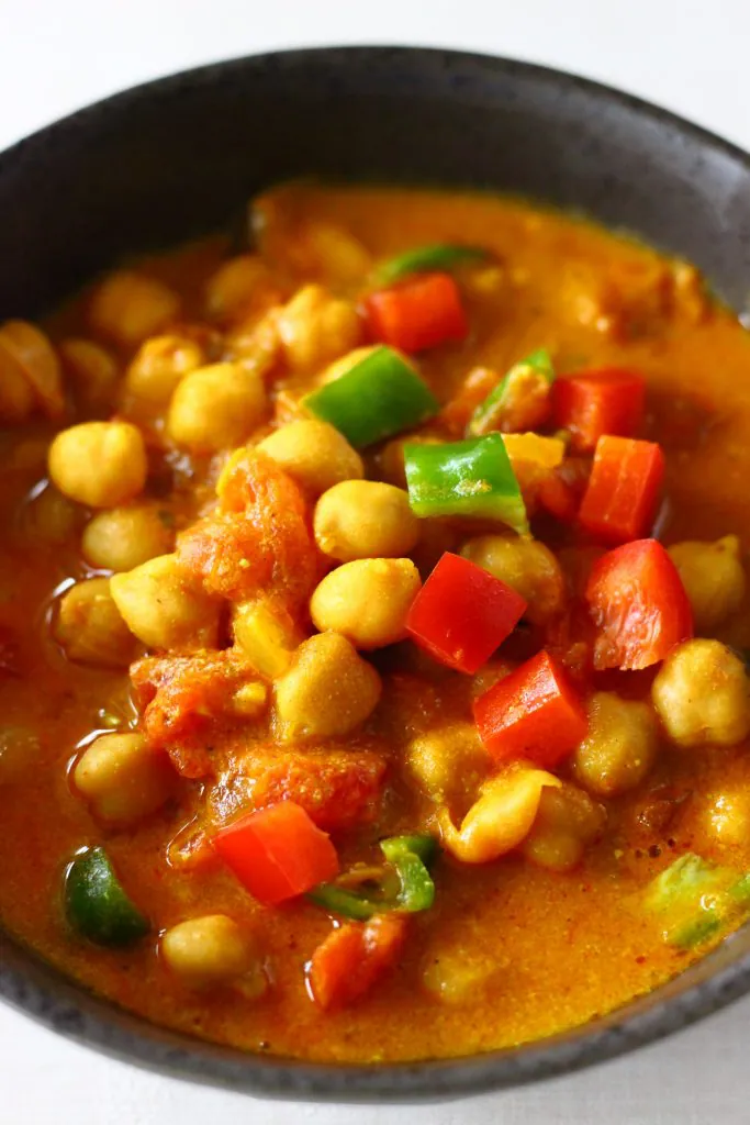 Red curry sauce with chickpeas, red peppers and green peppers in a black bowl against a white background
