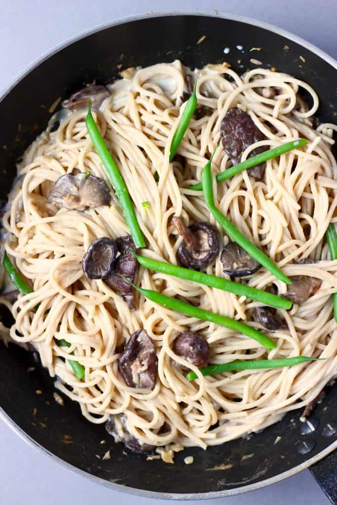 Photo of a black saucepan with spaghetti, mushrooms and green beans