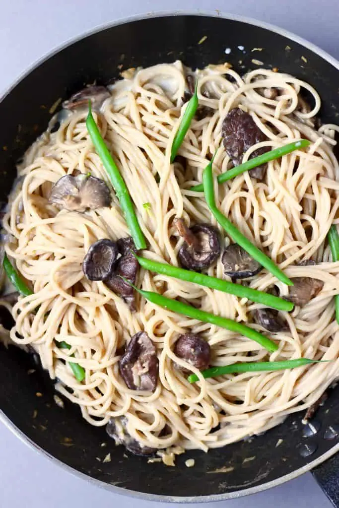 Photo of a black saucepan with spaghetti, mushrooms and green beans