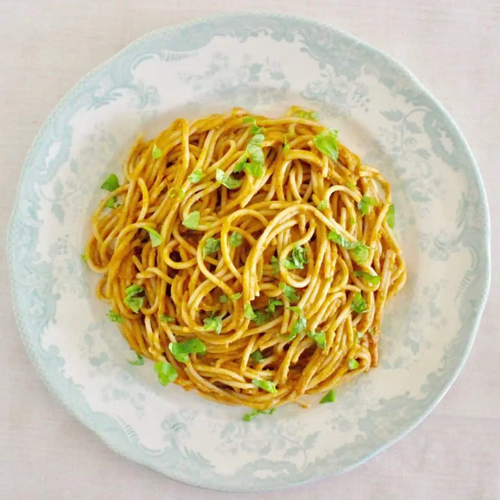 Spaghetti in a tomato sauce topped with basil on a white plate with a blue rim against a white background
