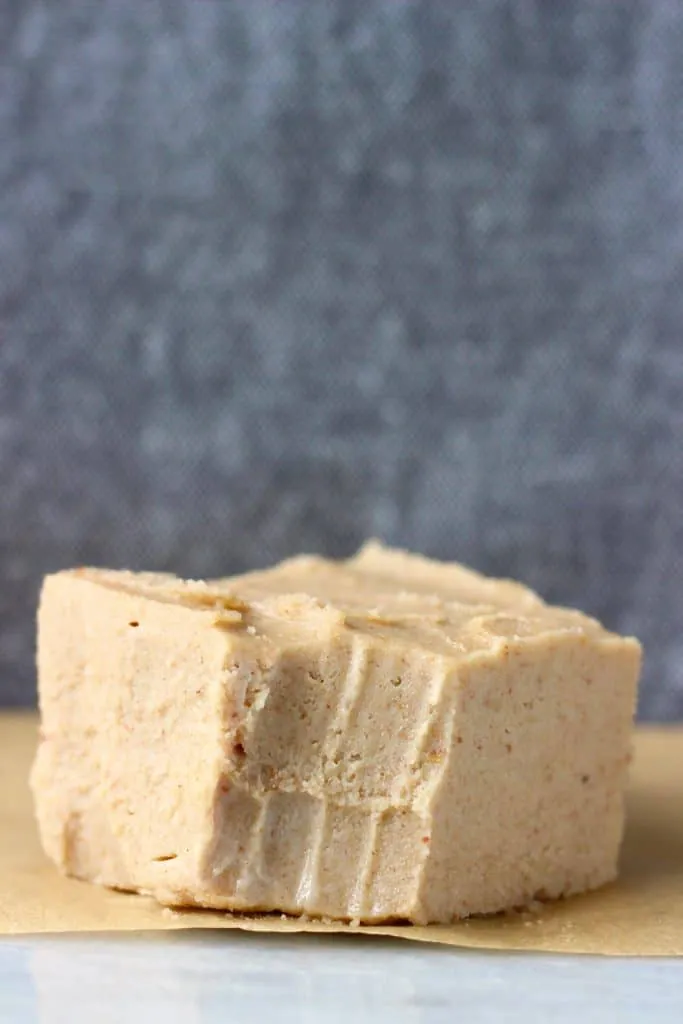 Photo of a square of caramel-coloured fudge with a bite taken out of it on a marble slab against a dark grey background