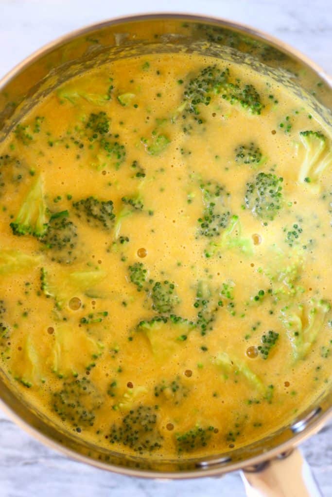 Yellow soup with broccoli in a silver saucepan against a marble background