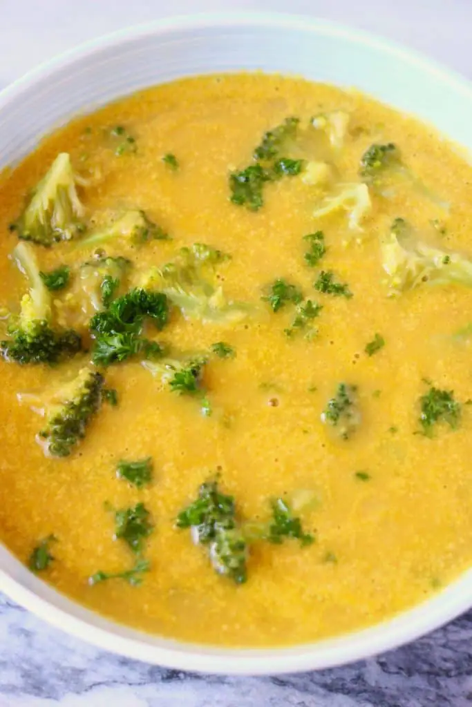 Yellow soup with broccoli in a blue bowl against a marble background