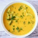 Yellow soup with broccoli in a blue bowl against a marble background