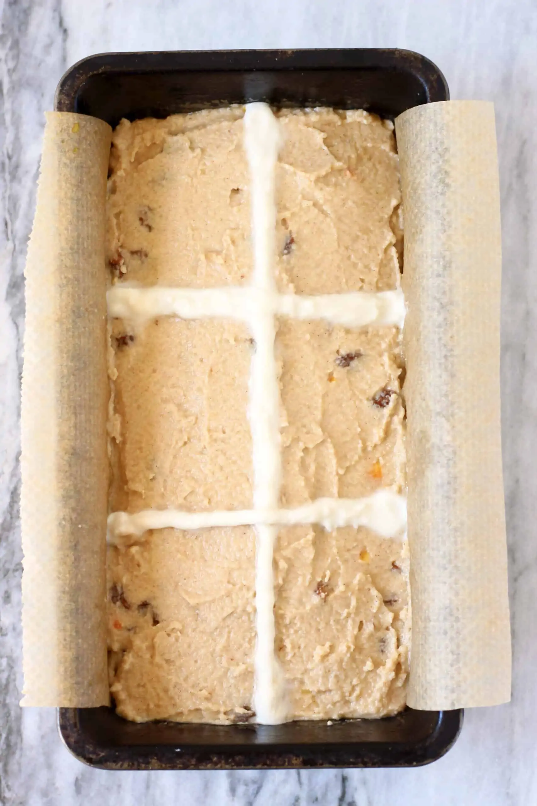 Raw gluten-free vegan hot cross bun loaf batter in a loaf tin with raw flour crosses piped on top