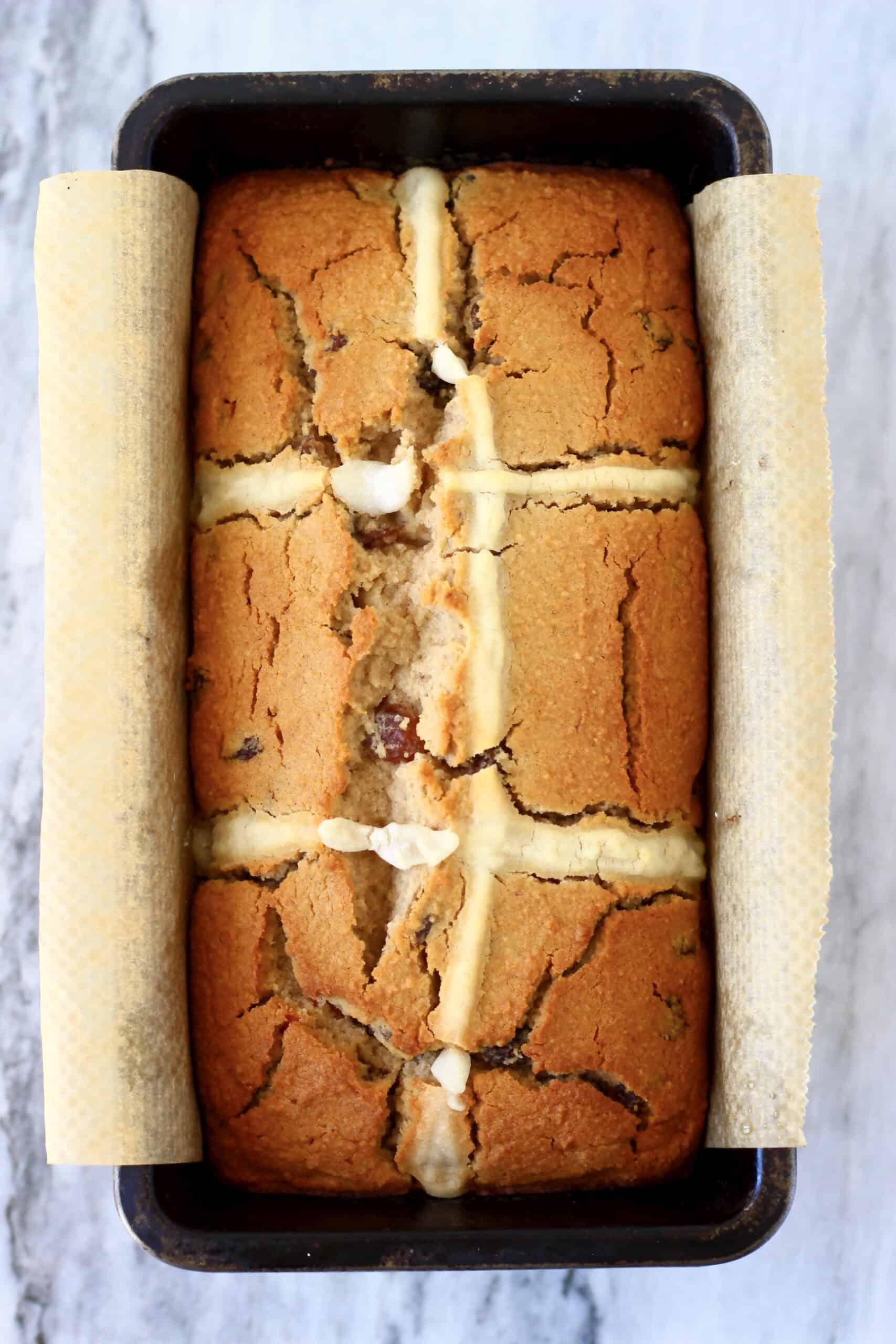 A gluten-free vegan hot cross bun loaf in a loaf tin lined with baking paper