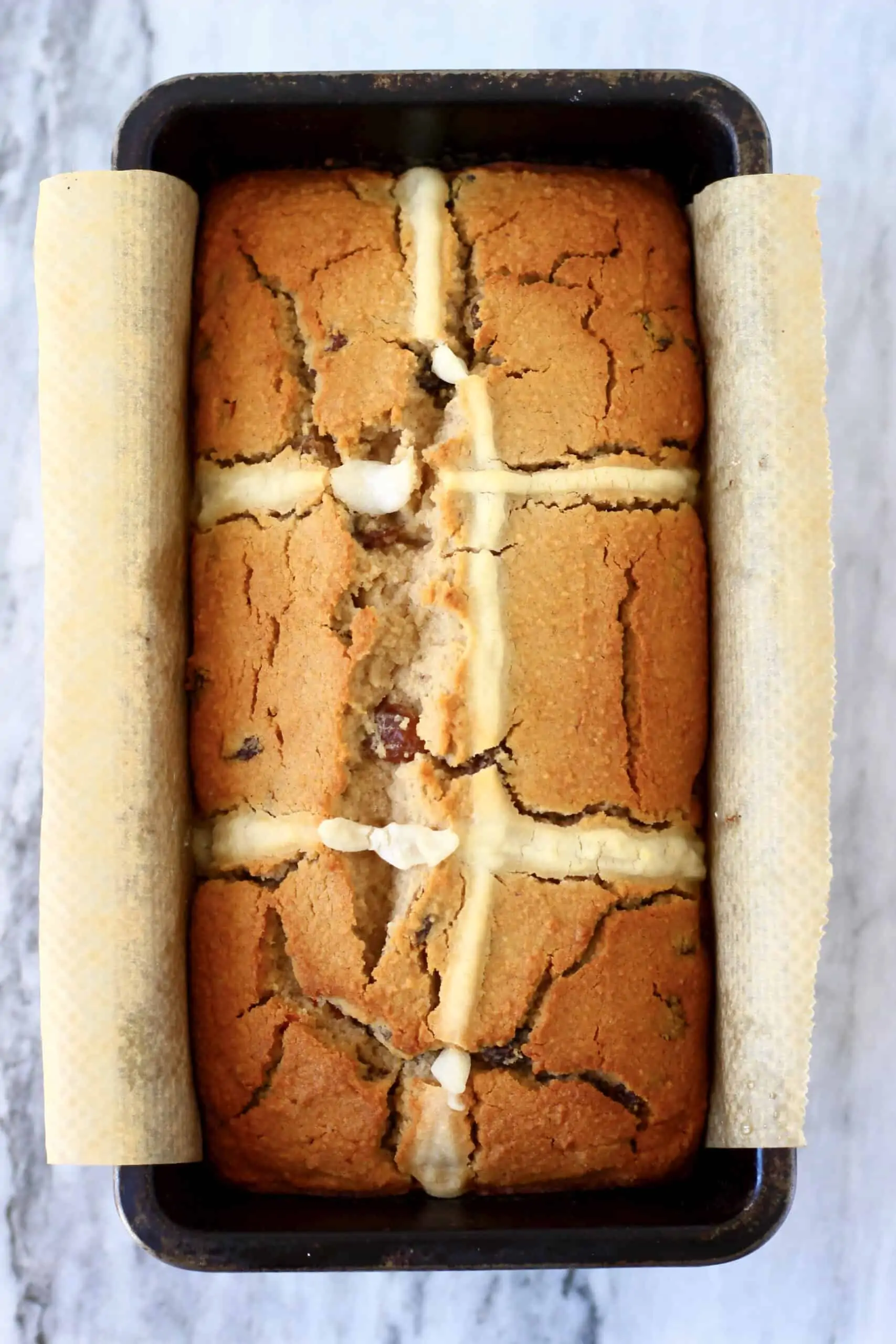 A gluten-free vegan hot cross bun loaf in a loaf tin lined with baking paper