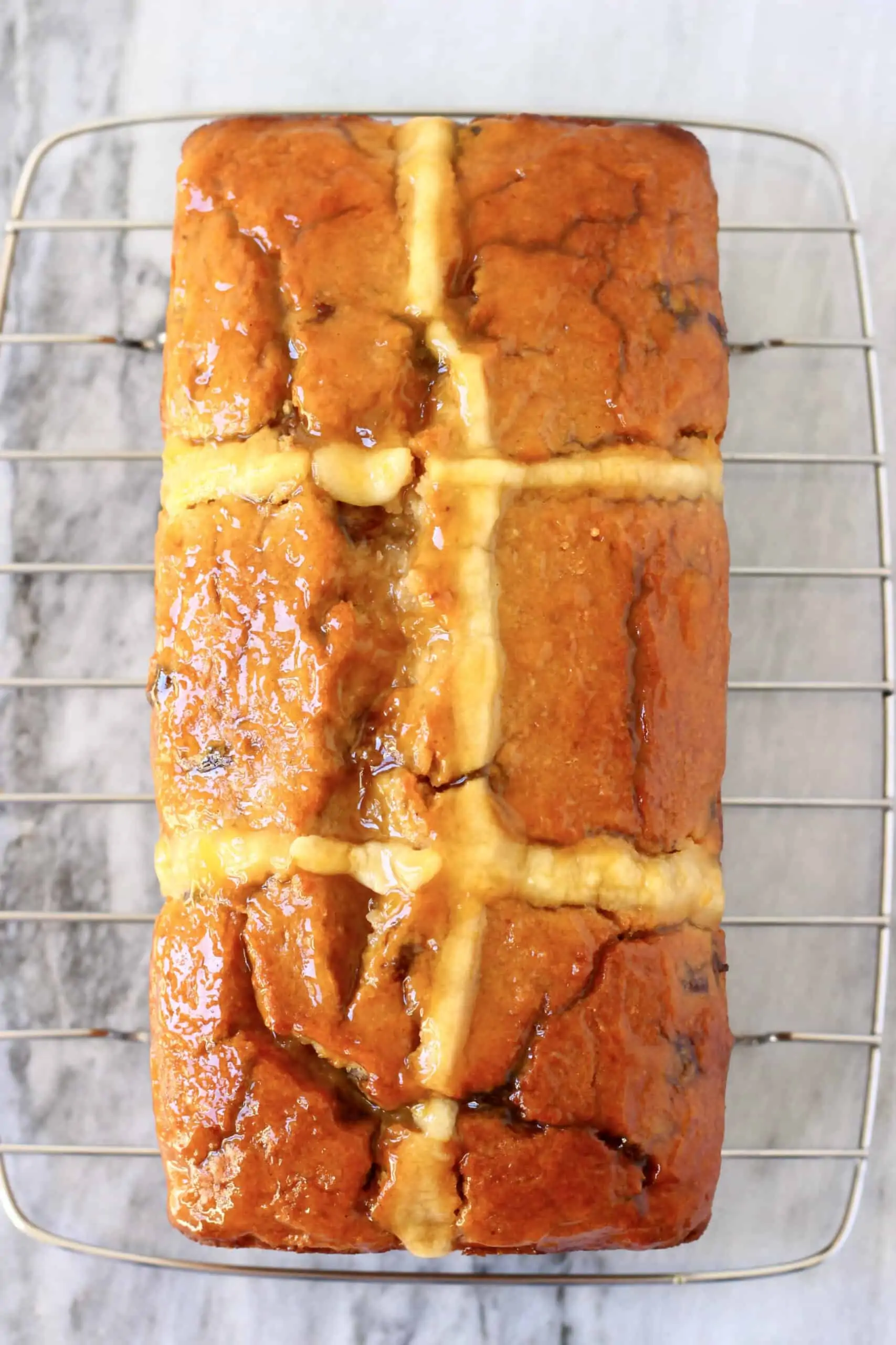 A gluten-free vegan hot cross bun loaf spread with apricot jam on a wire rack