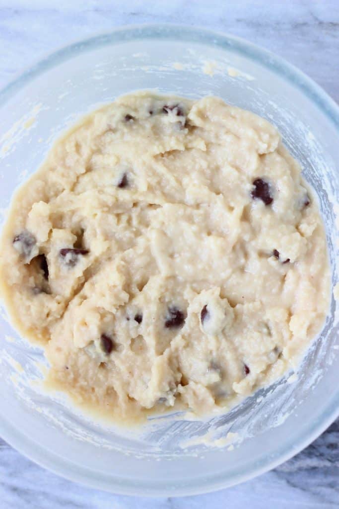 Raw muffin batter with chocolate chips in a glass mixing bowl against a marble background