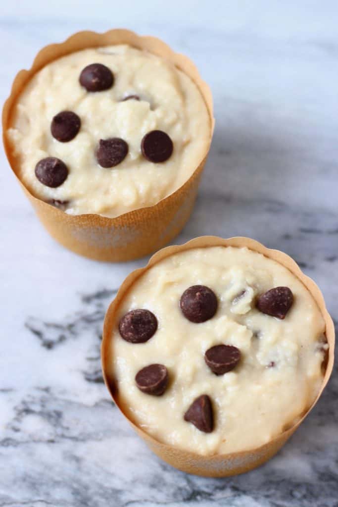 Raw muffin batter with chocolate chips in muffin cases against a marble background