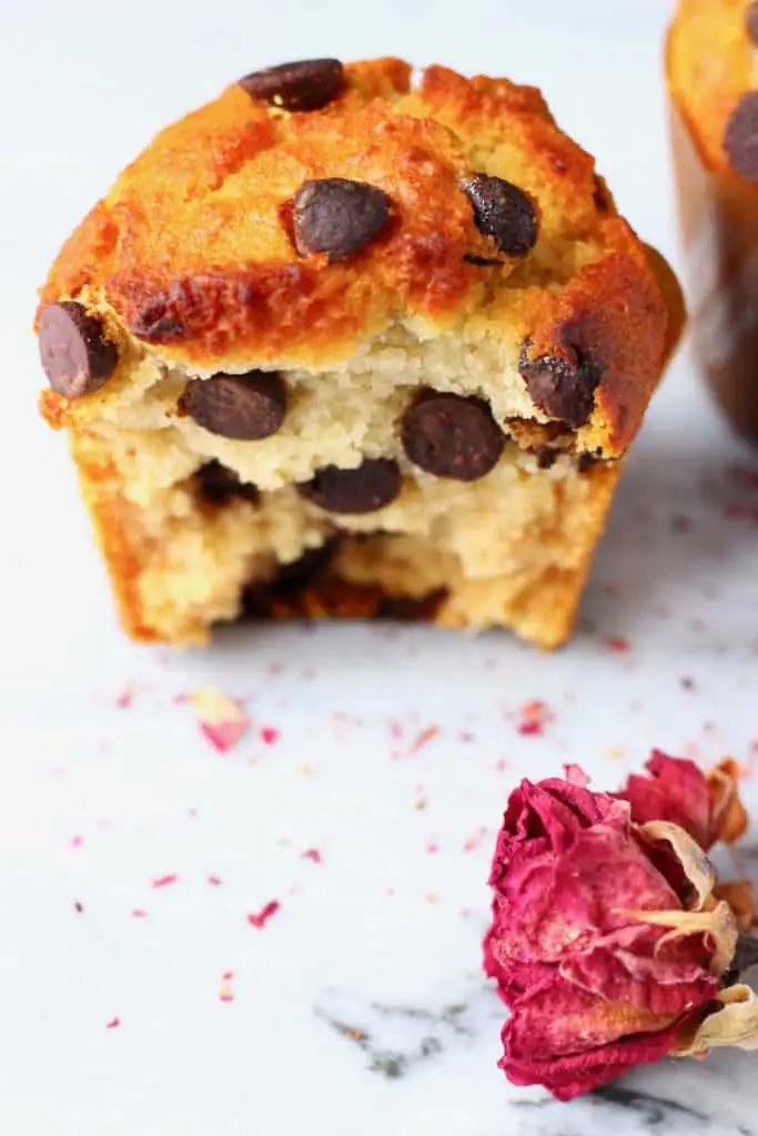 Half of a chocolate chip muffin on a marble slab with a dried rose