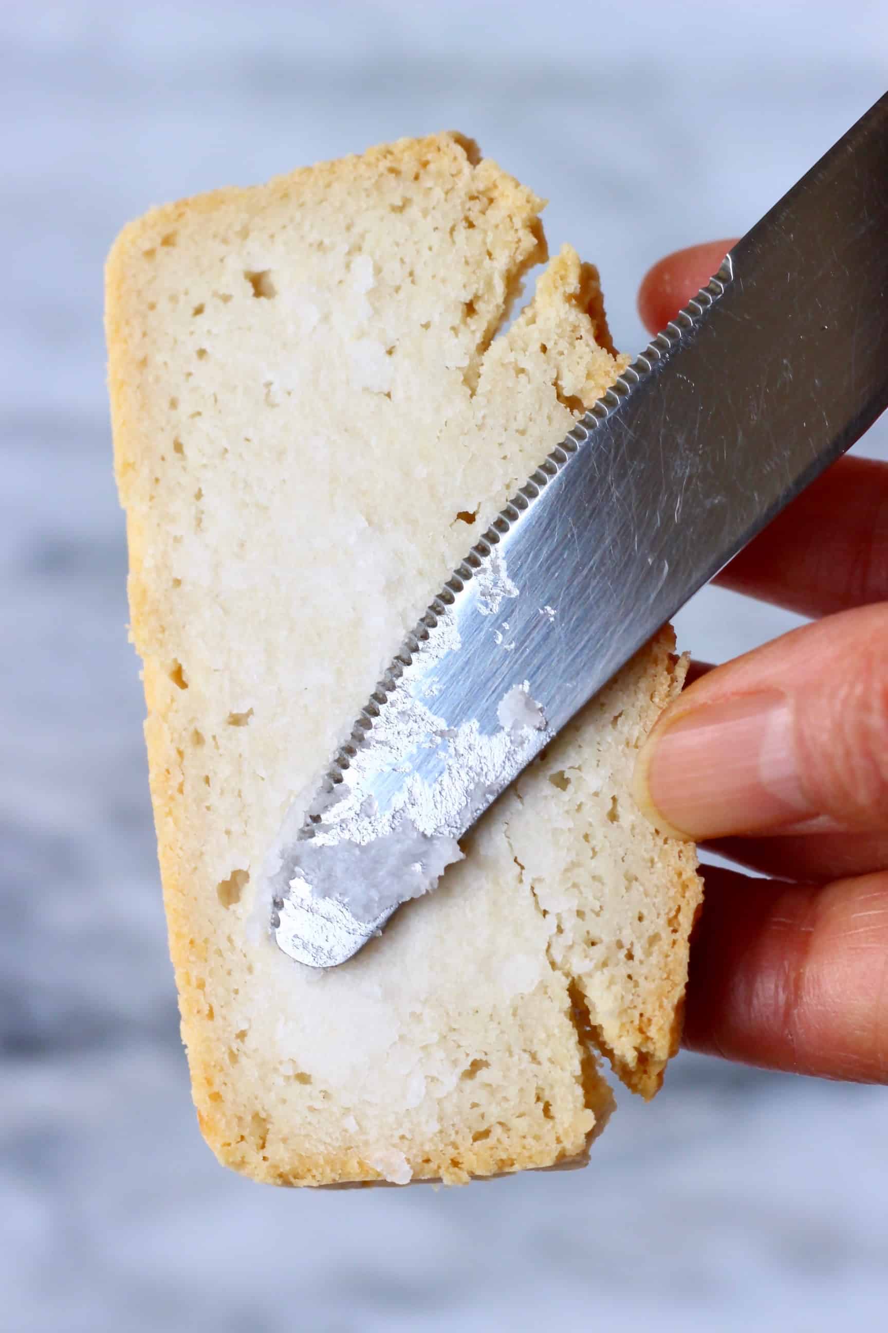 A slice of bread with coconut oil being spread on it with a silver knife 