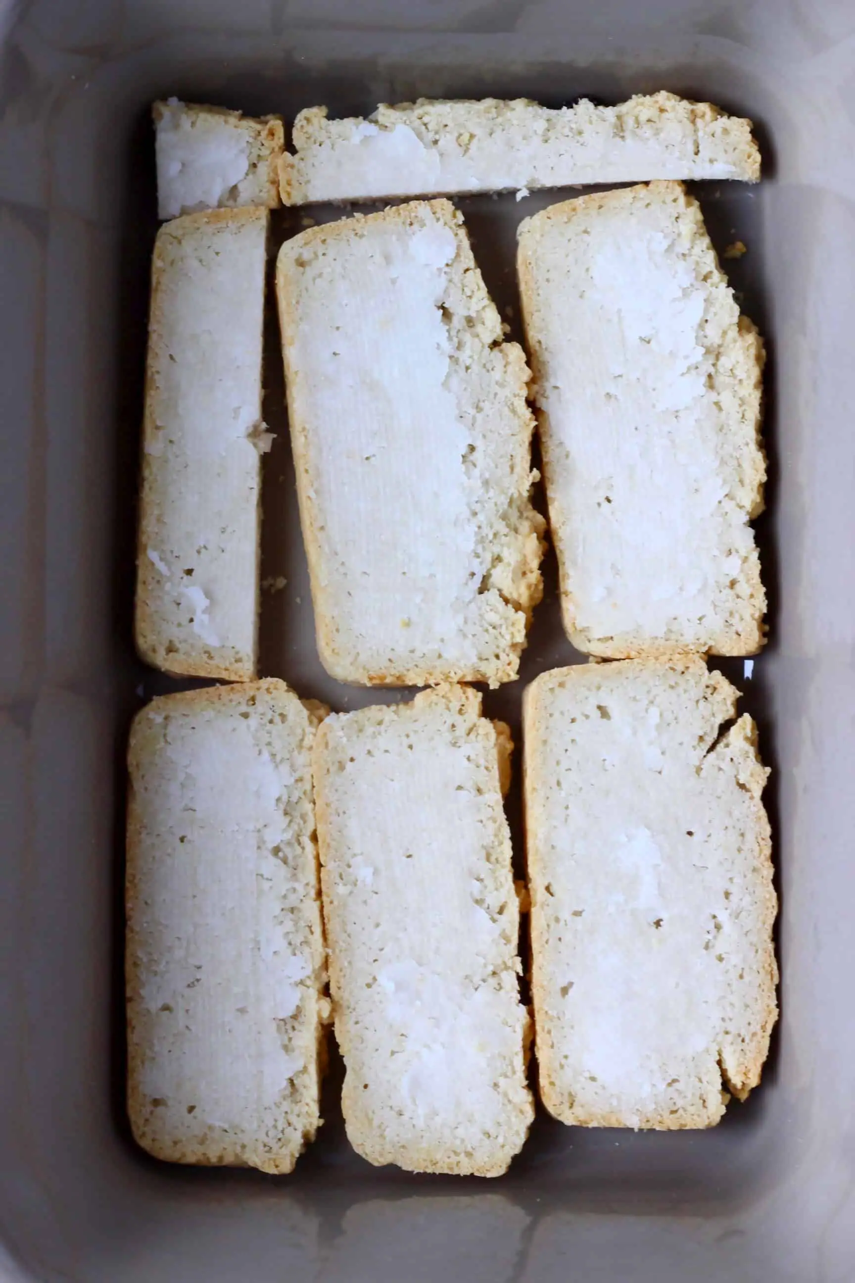 Slices of bread spread with coconut oil in a grey rectangular baking dish