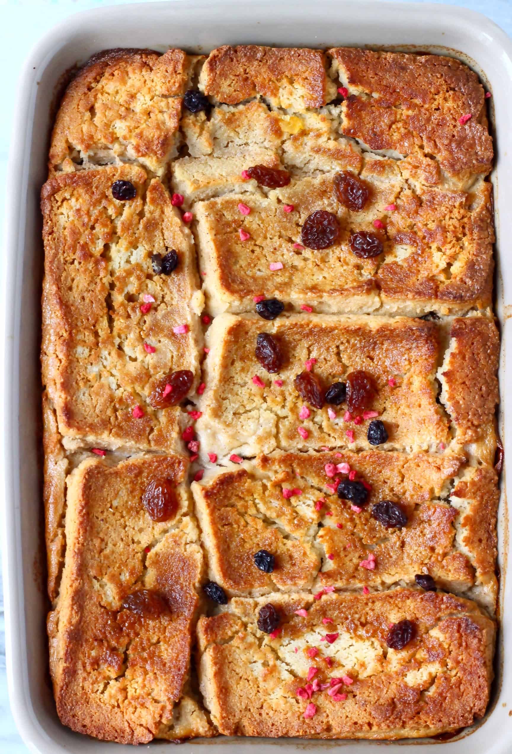 Vegan bread pudding in a grey rectangular baking dish sprinkled with raisins