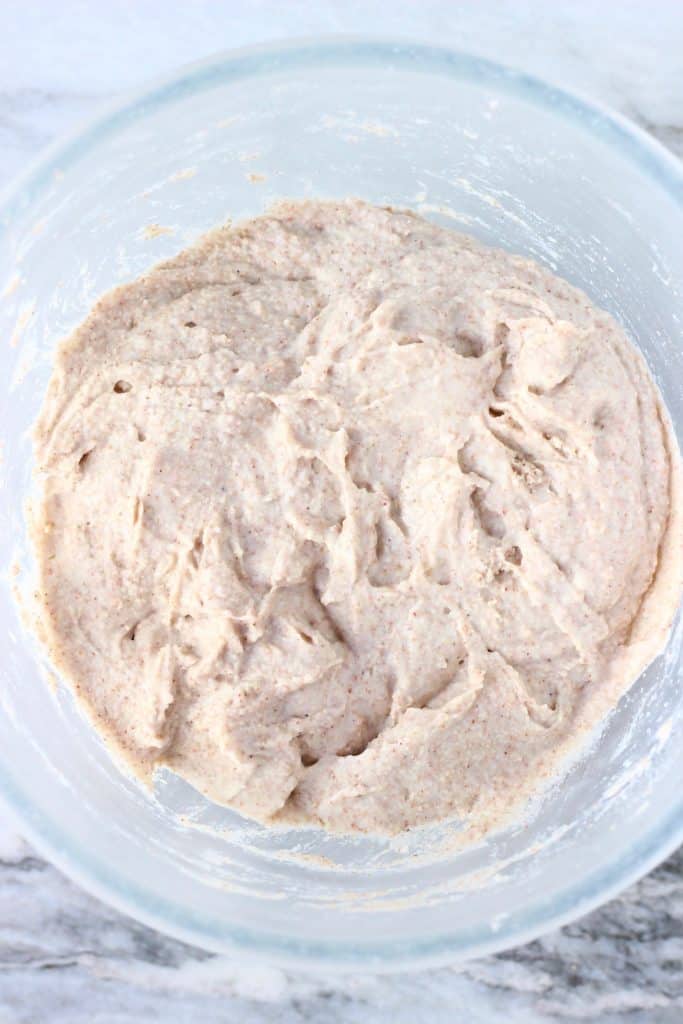 Raw buckwheat pancake batter in a glass mixing bowl against a marble background