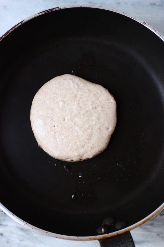 A buckwheat pancake being cooked on a black frying pan against a marble background