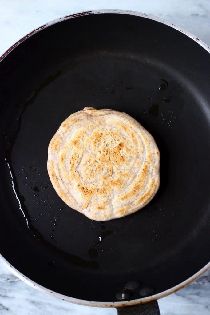 A buckwheat pancake being cooked on a black frying pan against a marble background