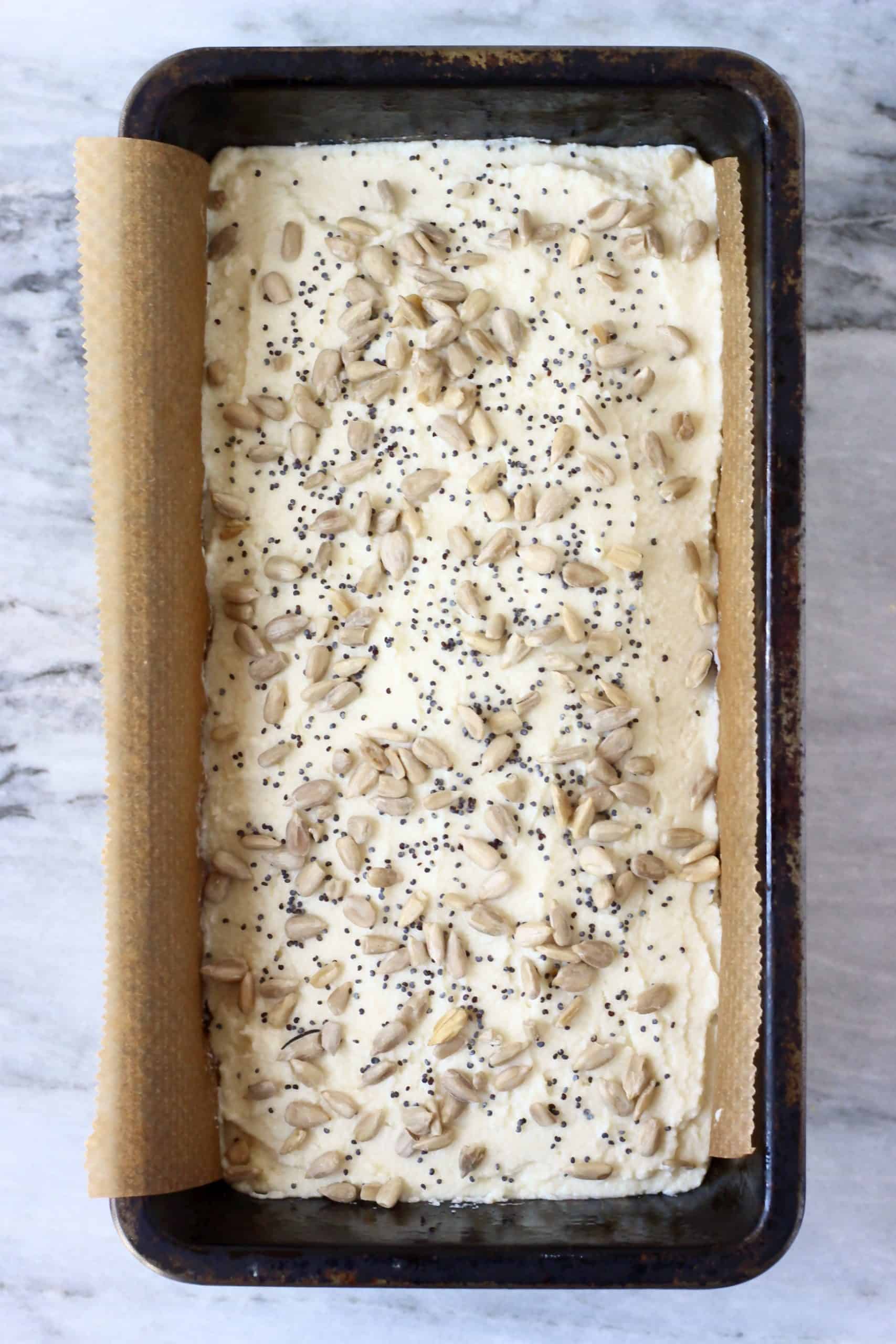 Raw coconut flour bread batter in a loaf tin sprinkled with sunflower seeds and poppy seeds