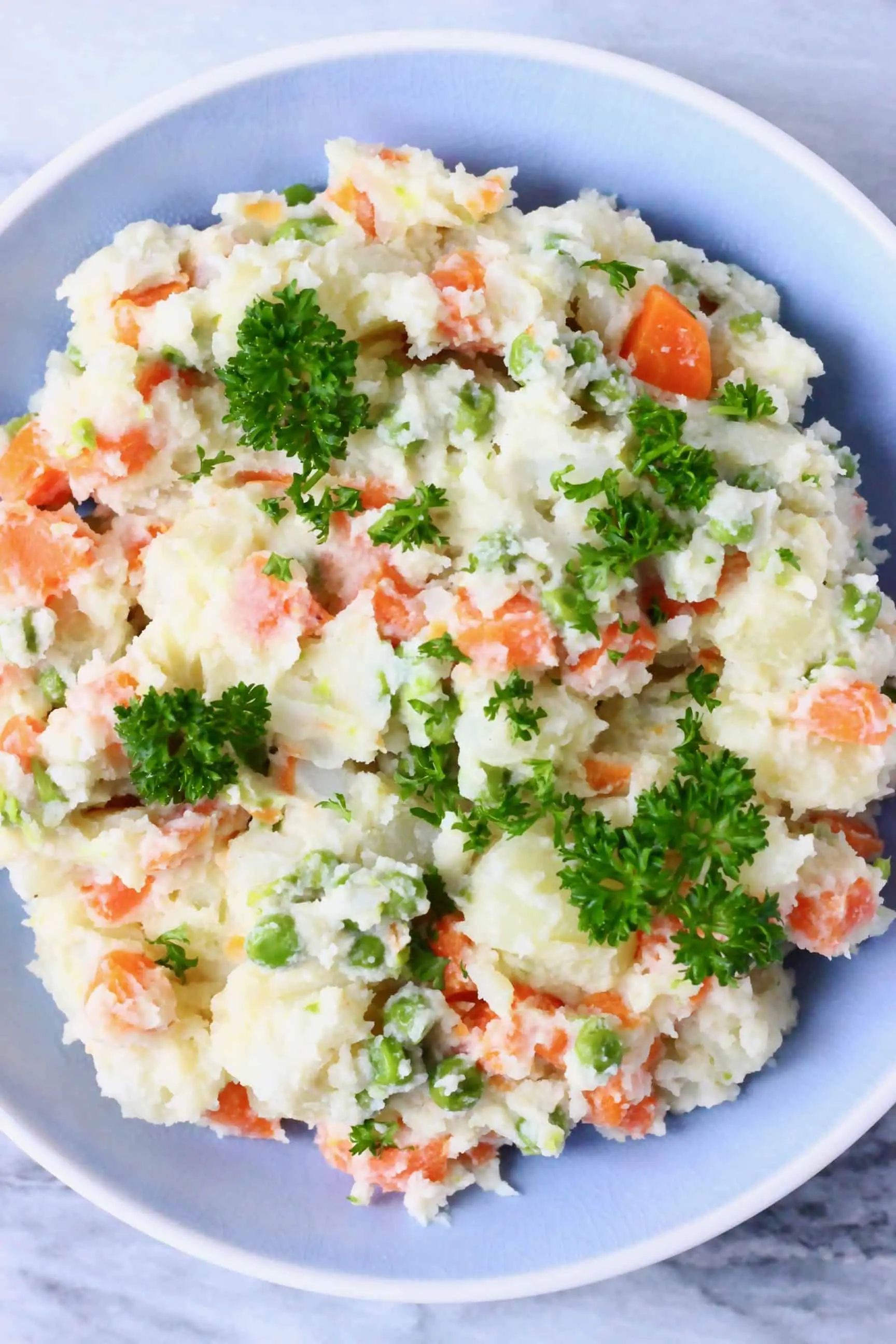 Potato salad with carrots, green peas and mayonnaise in a blue bowl against a marble background