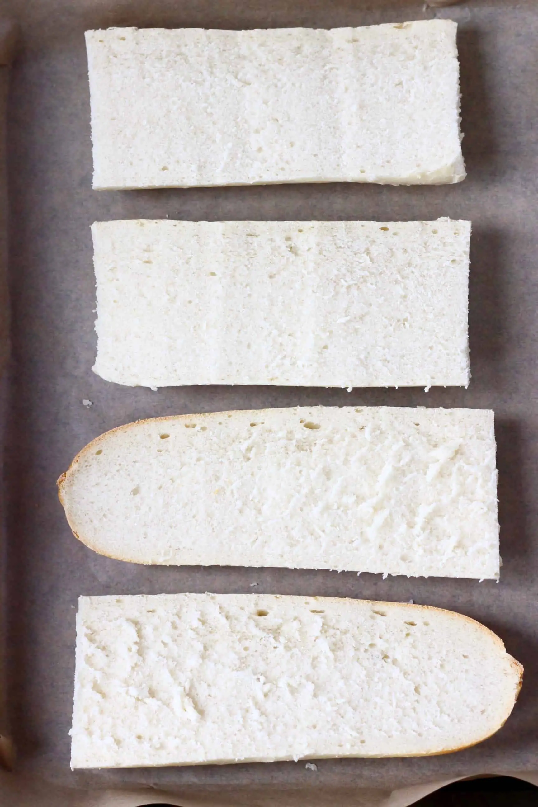 Four pieces of sliced white baguette on a sheet of baking paper