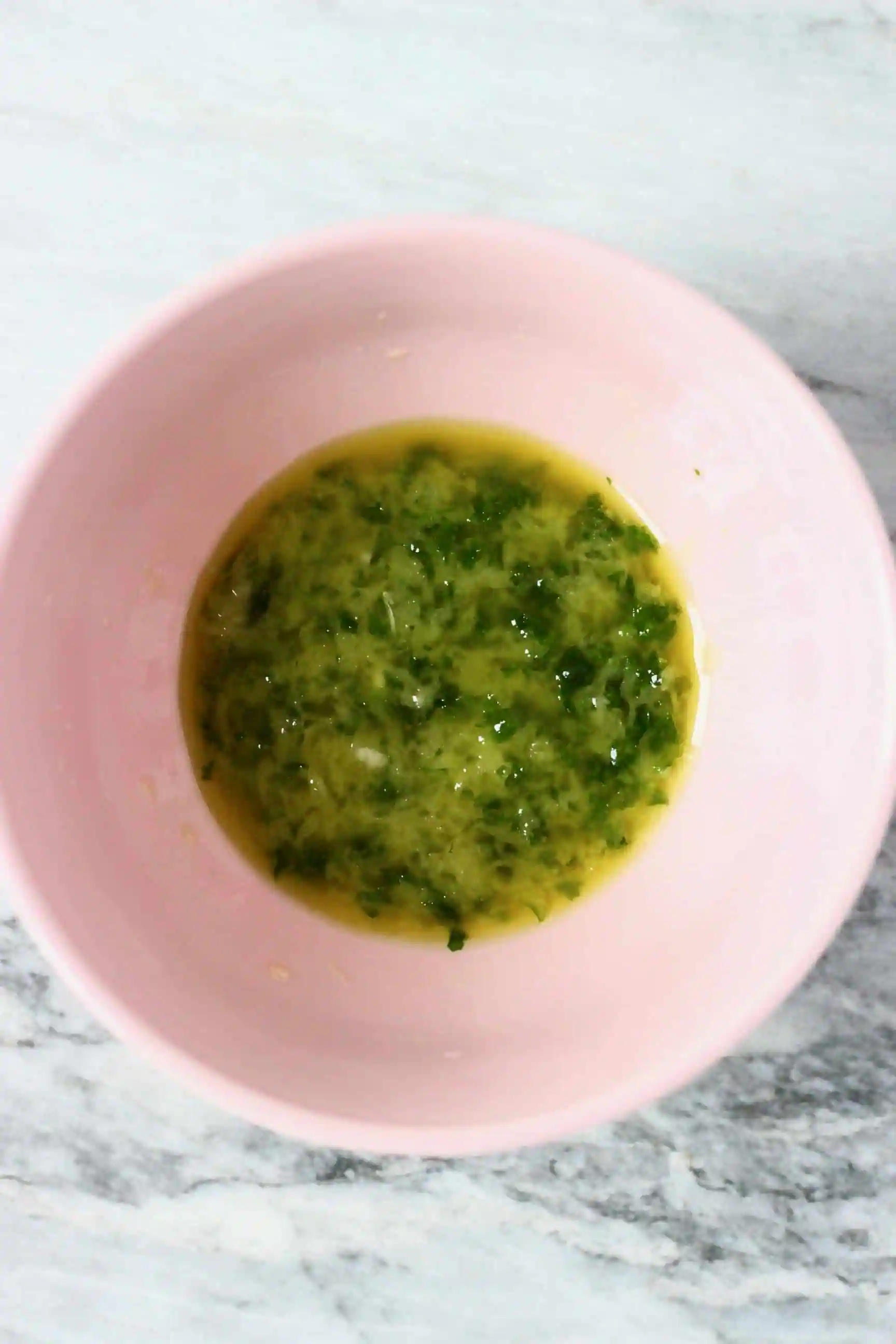 Oil, grated garlic and chopped green herbs in a pink bowl 