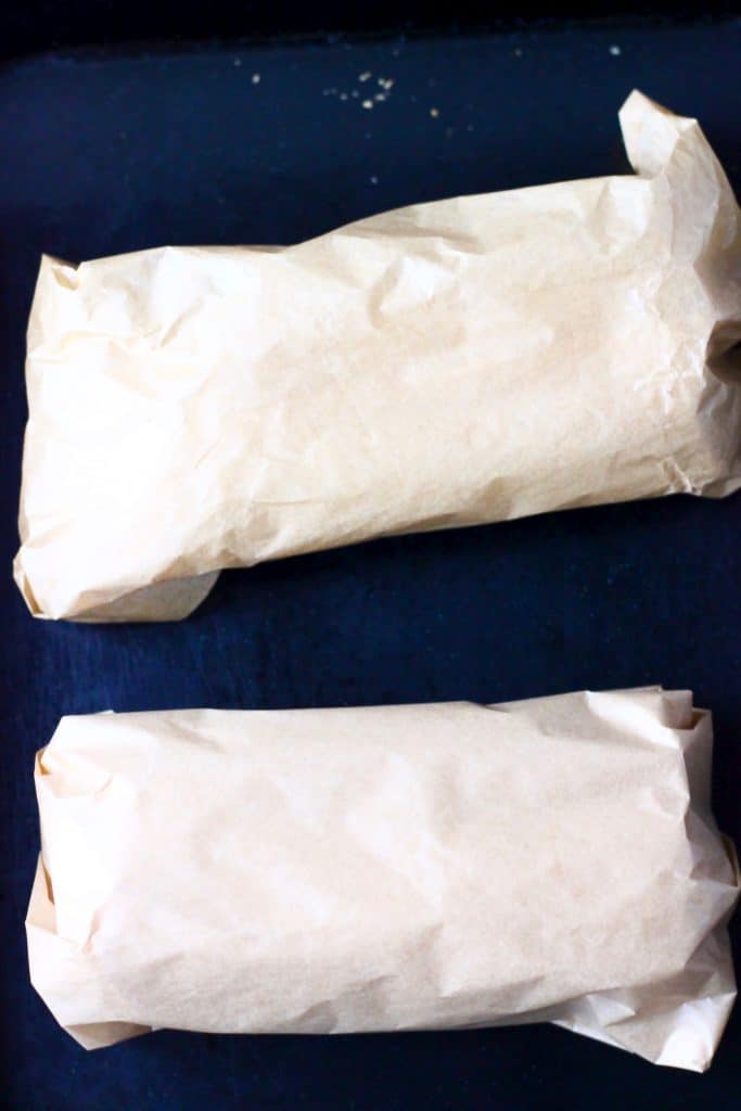 Two parcels wrapped in brown baking paper on a black baking tray