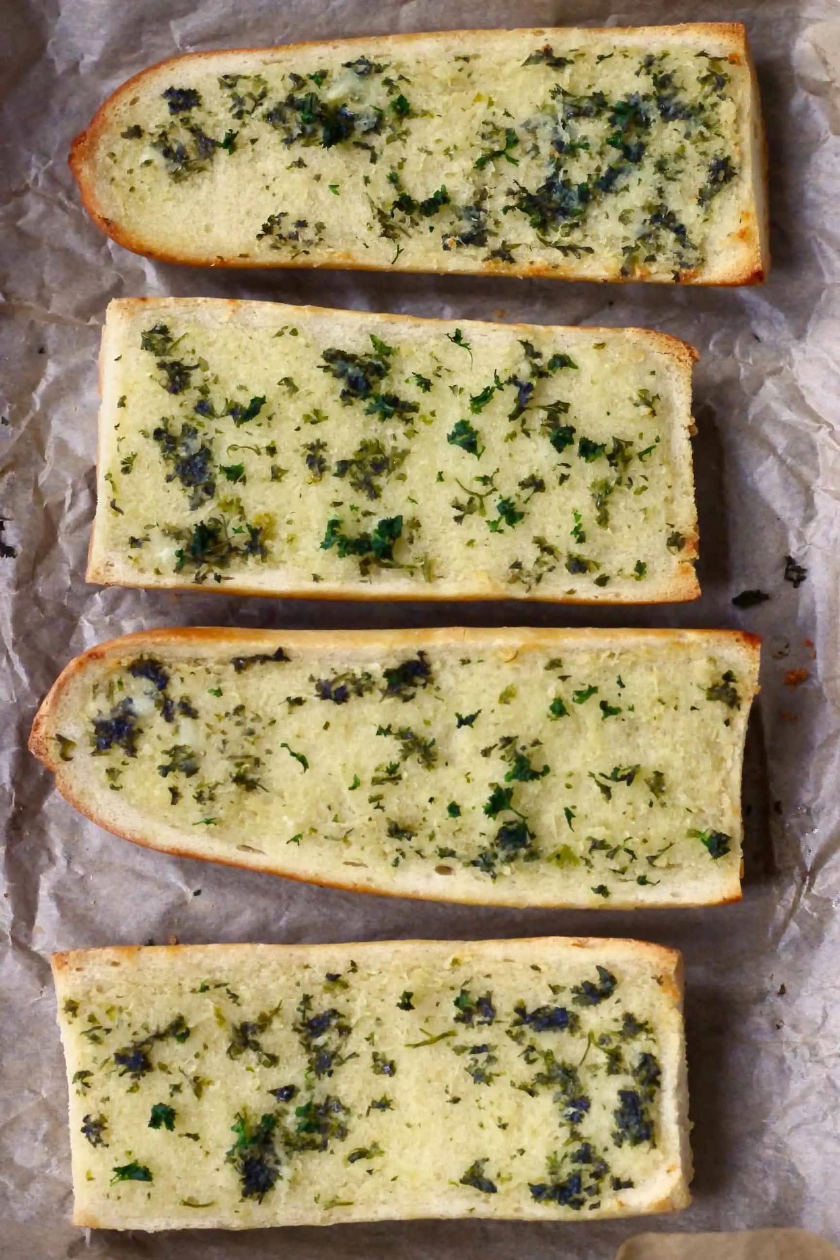 Four pieces of vegan garlic bread on a sheet of baking paper