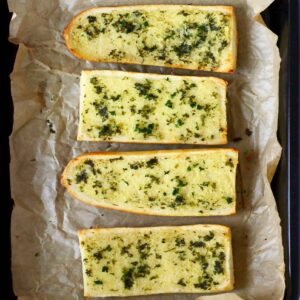 Four pieces of vegan garlic bread on a sheet of brown baking paper