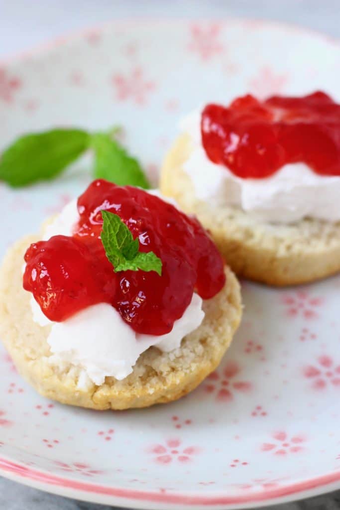 Two scone halves topped with white cream and strawberry jam decorate with mint leaves on a white plate with pink flowers