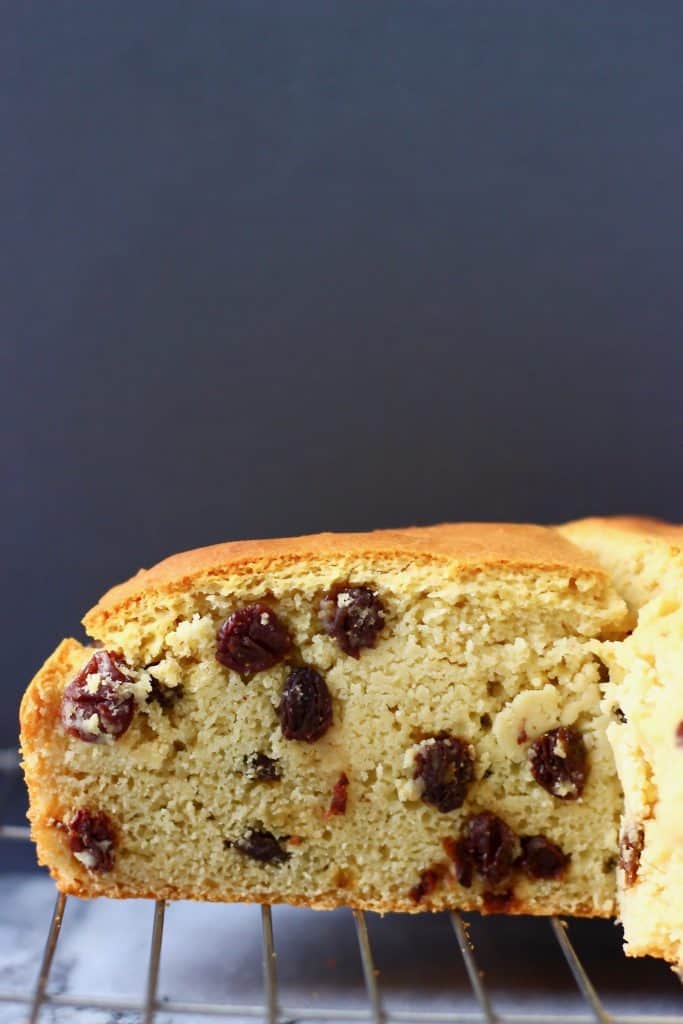 A loaf of bread filled with raisins on a wire rack against a dark grey background