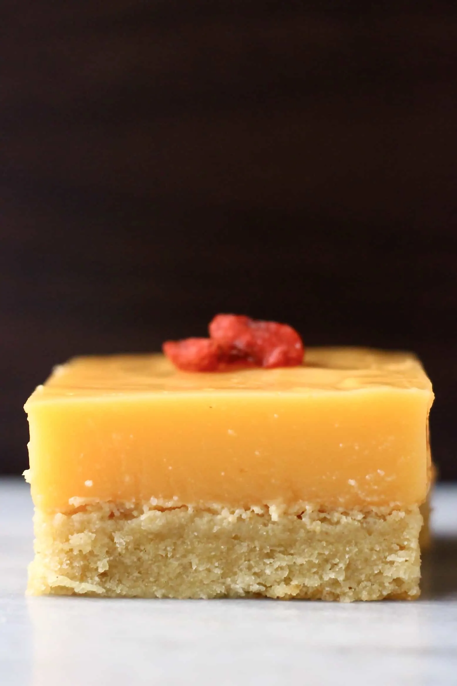 A lemon bar topped with goji berries on a marble slab