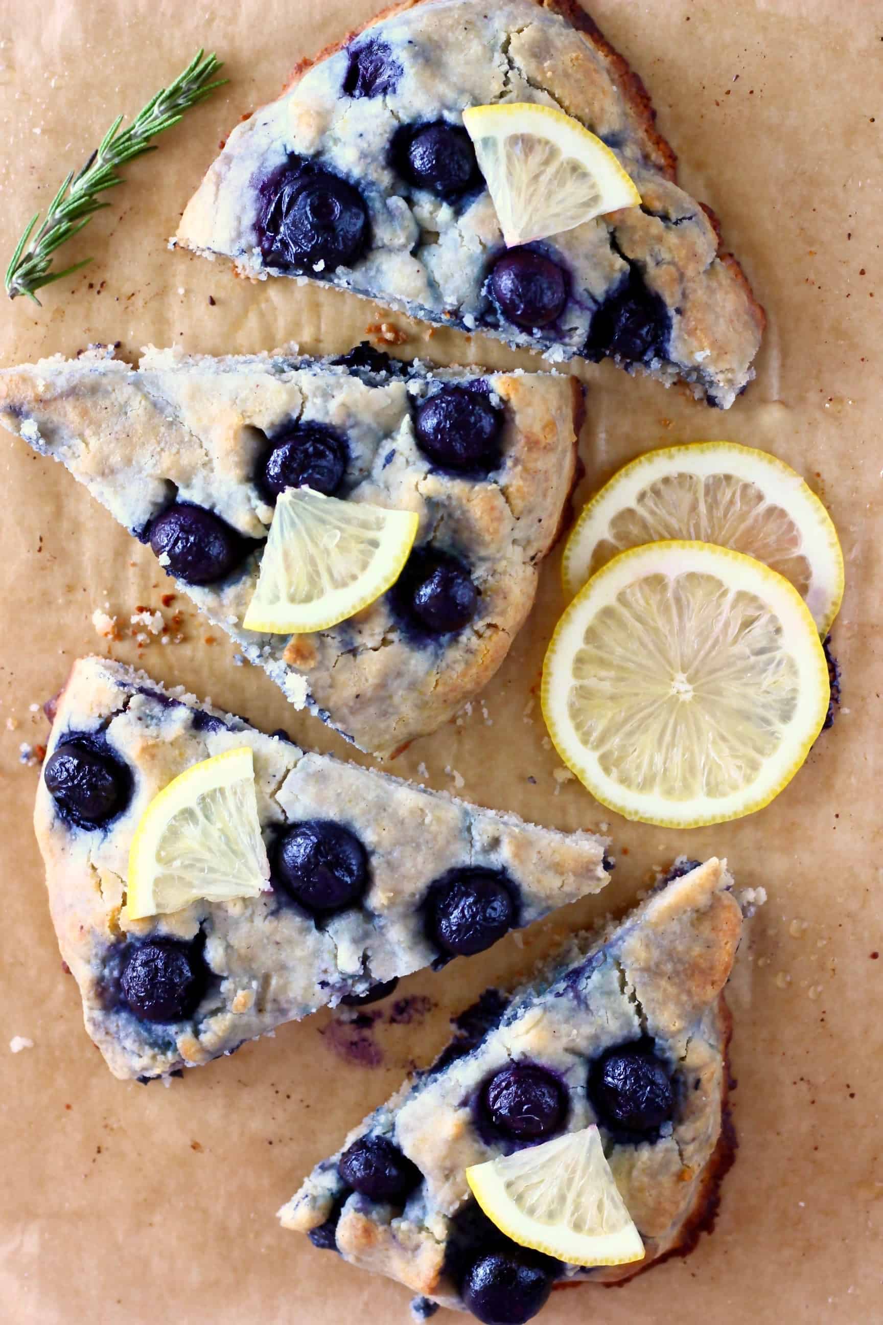 Photo of four triangular blueberry scones topped with lemon wedges on a sheet of brown baking paper