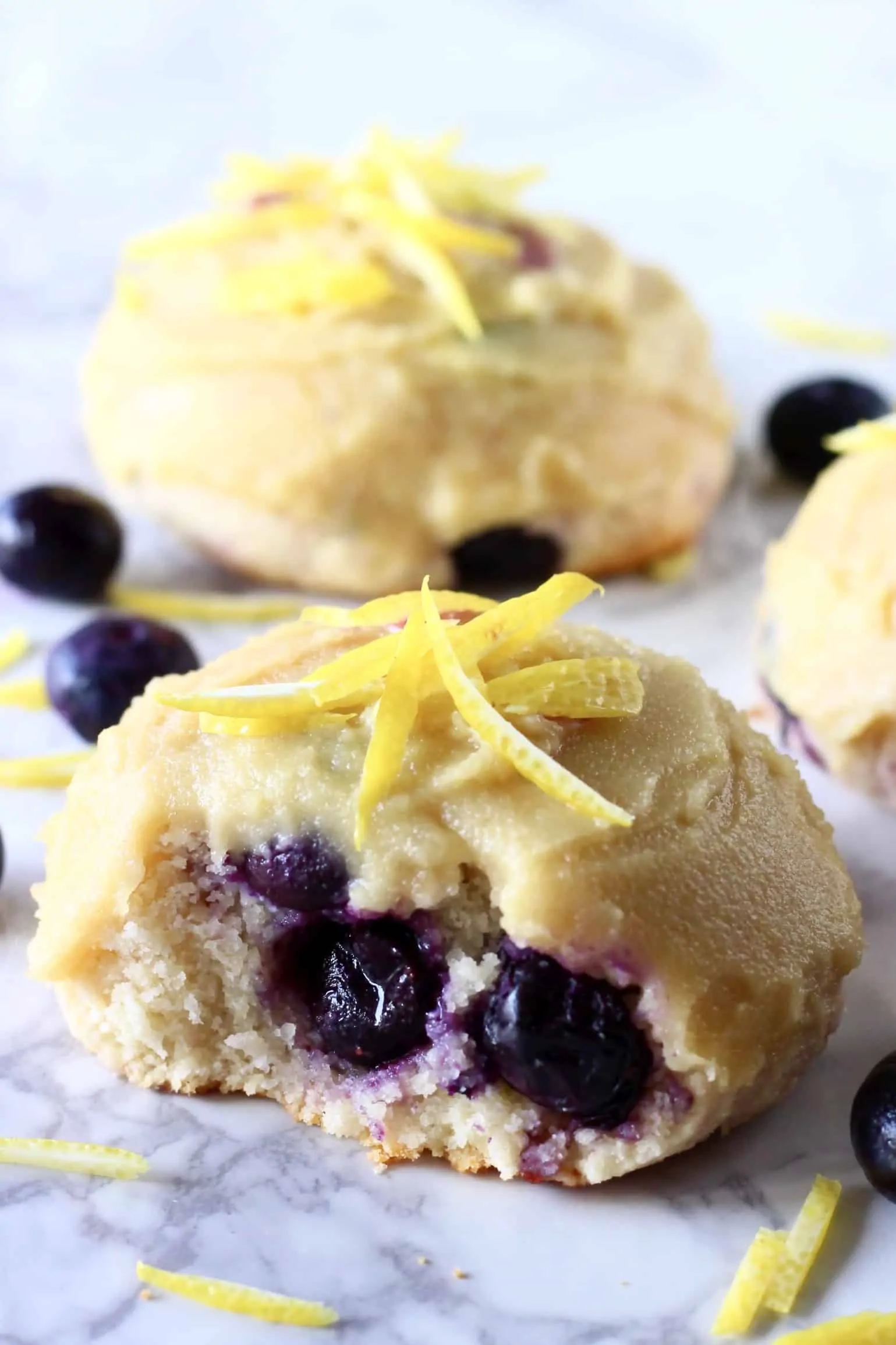 Three lemon blueberry cookies with frosting and a bite taken out of one