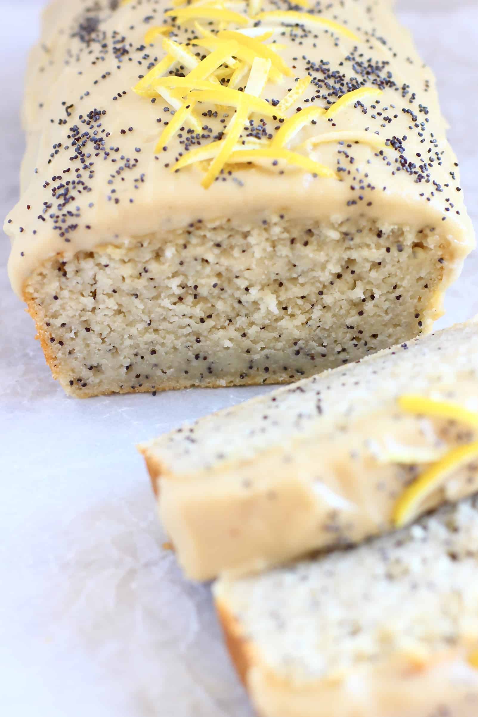 Lemon poppy seed loaf cake topped with frosting, lemon zest and poppy seeds with two slices next to it