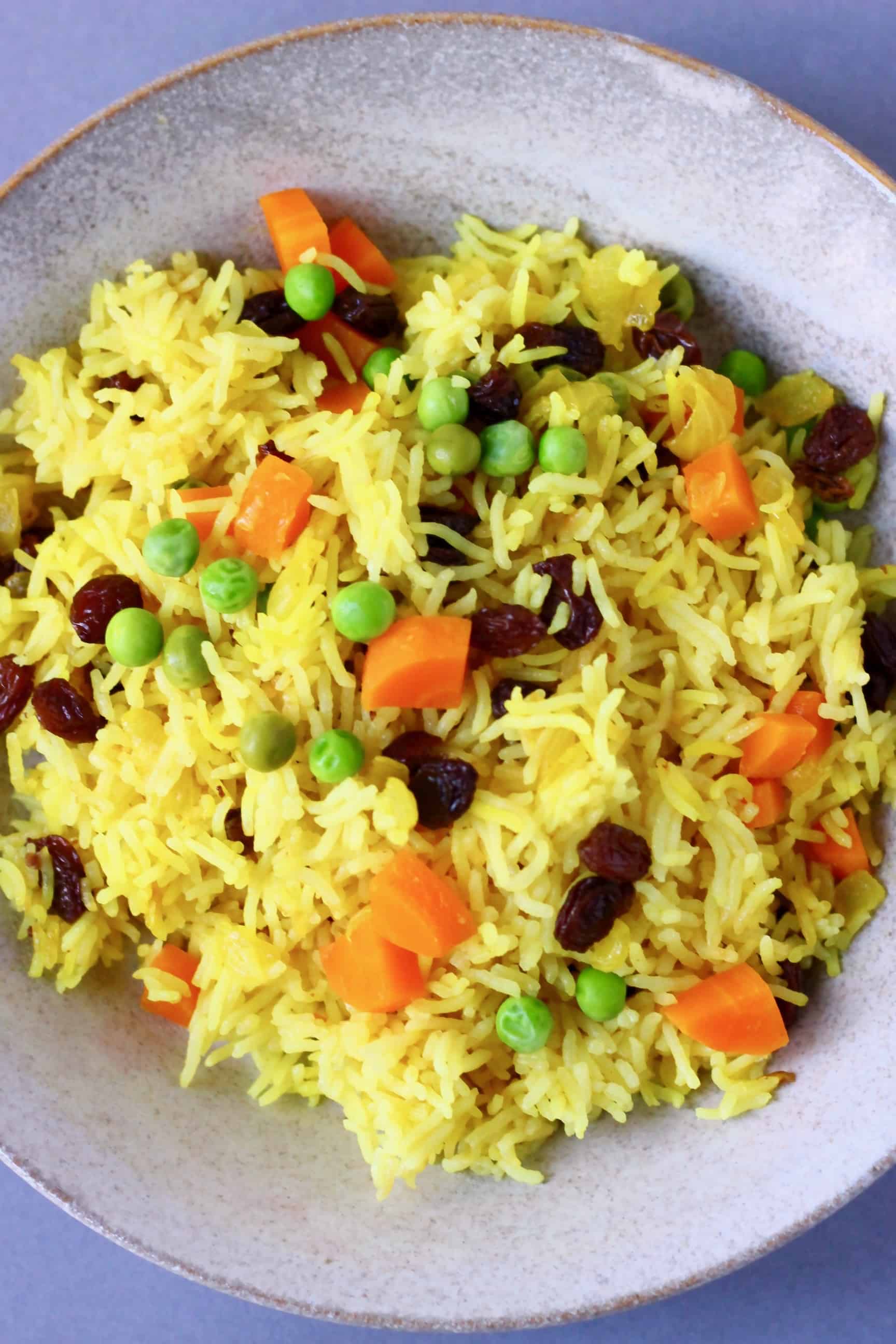 Yellow turmeric rice with vegetables in a ceramic bowl against a grey background