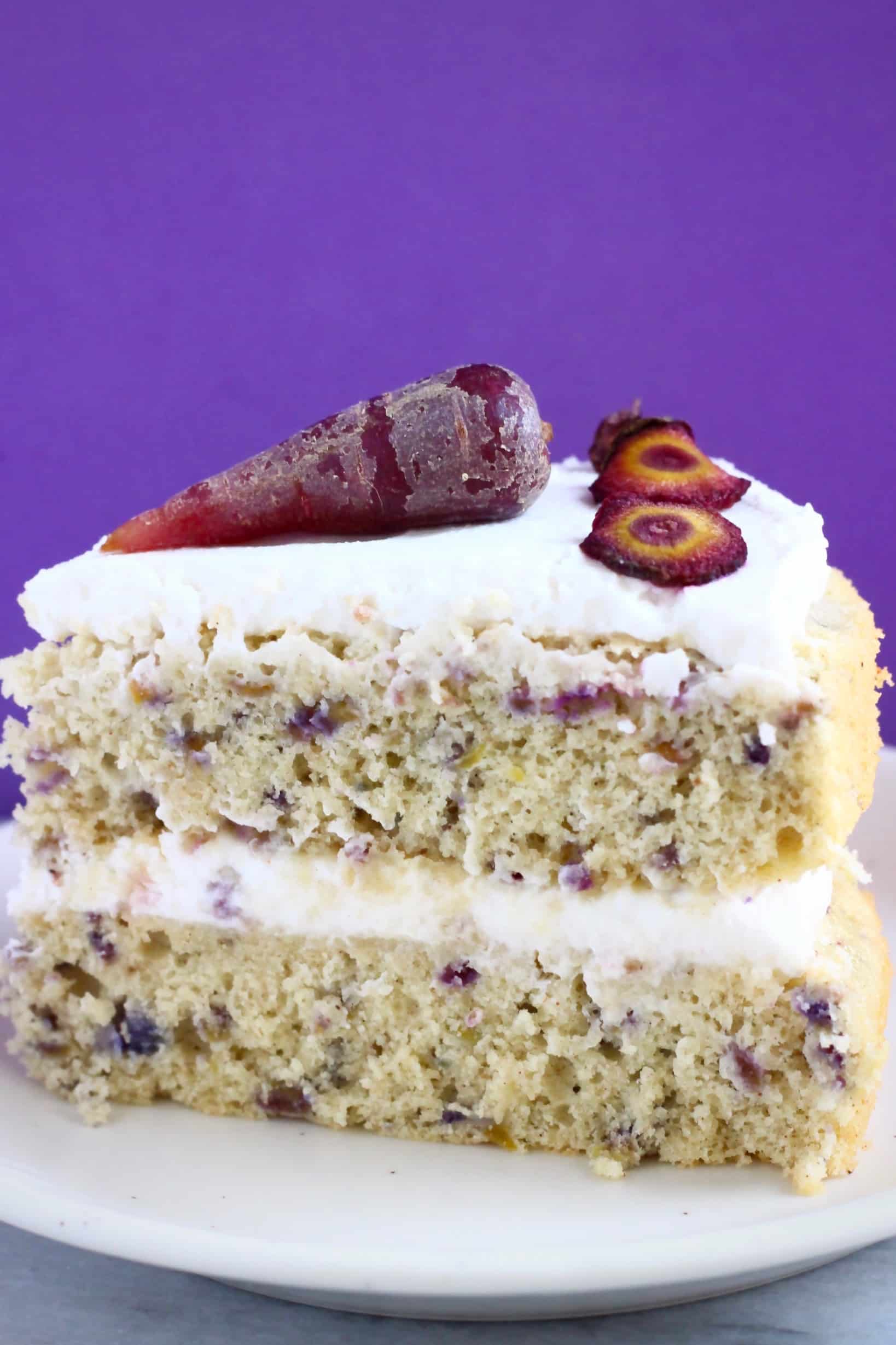 A slice of purple carrot cake on a white plate against a purple background