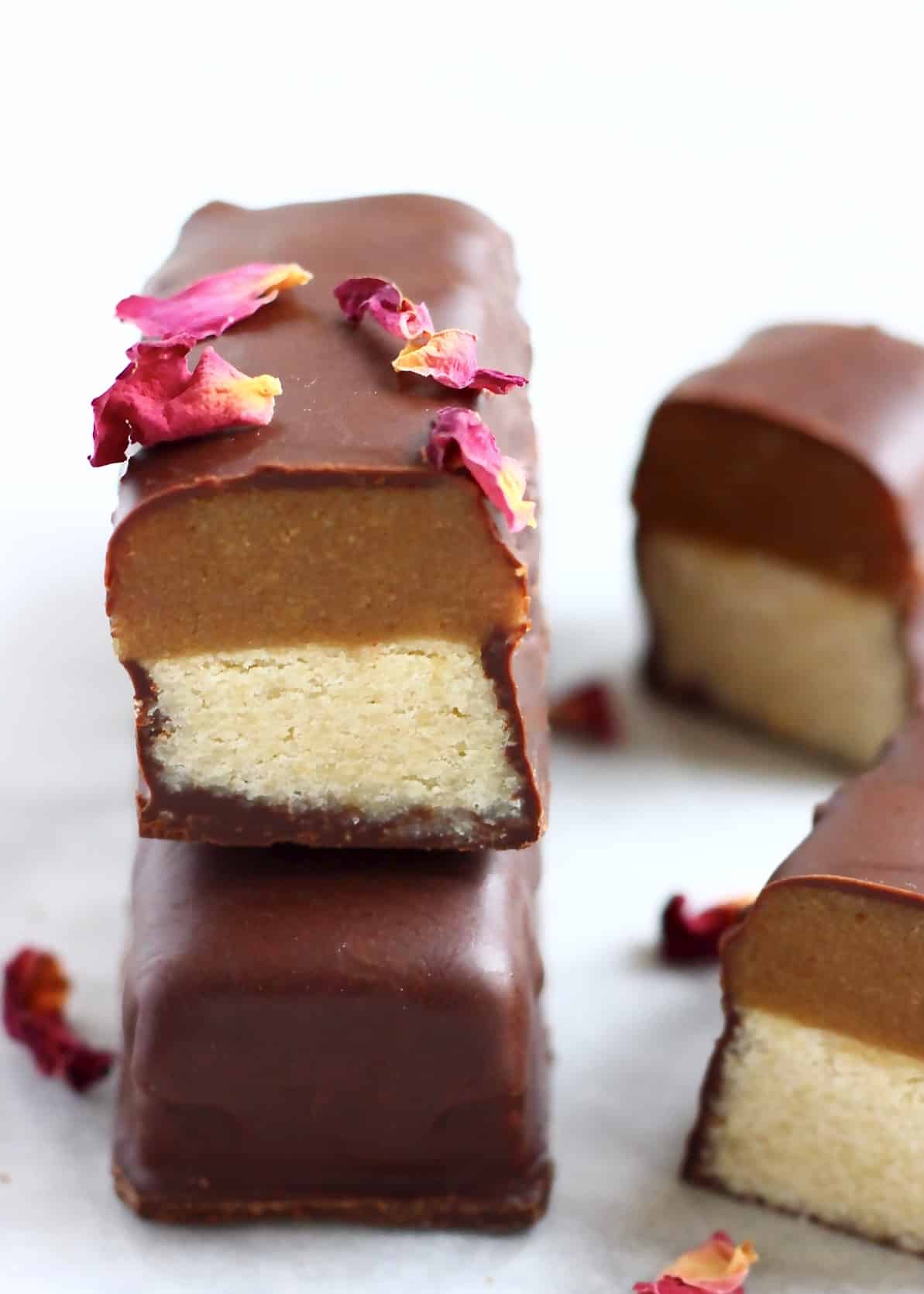 A vegan twix bar cut in half on top of a whole bar decorated with rose petals
