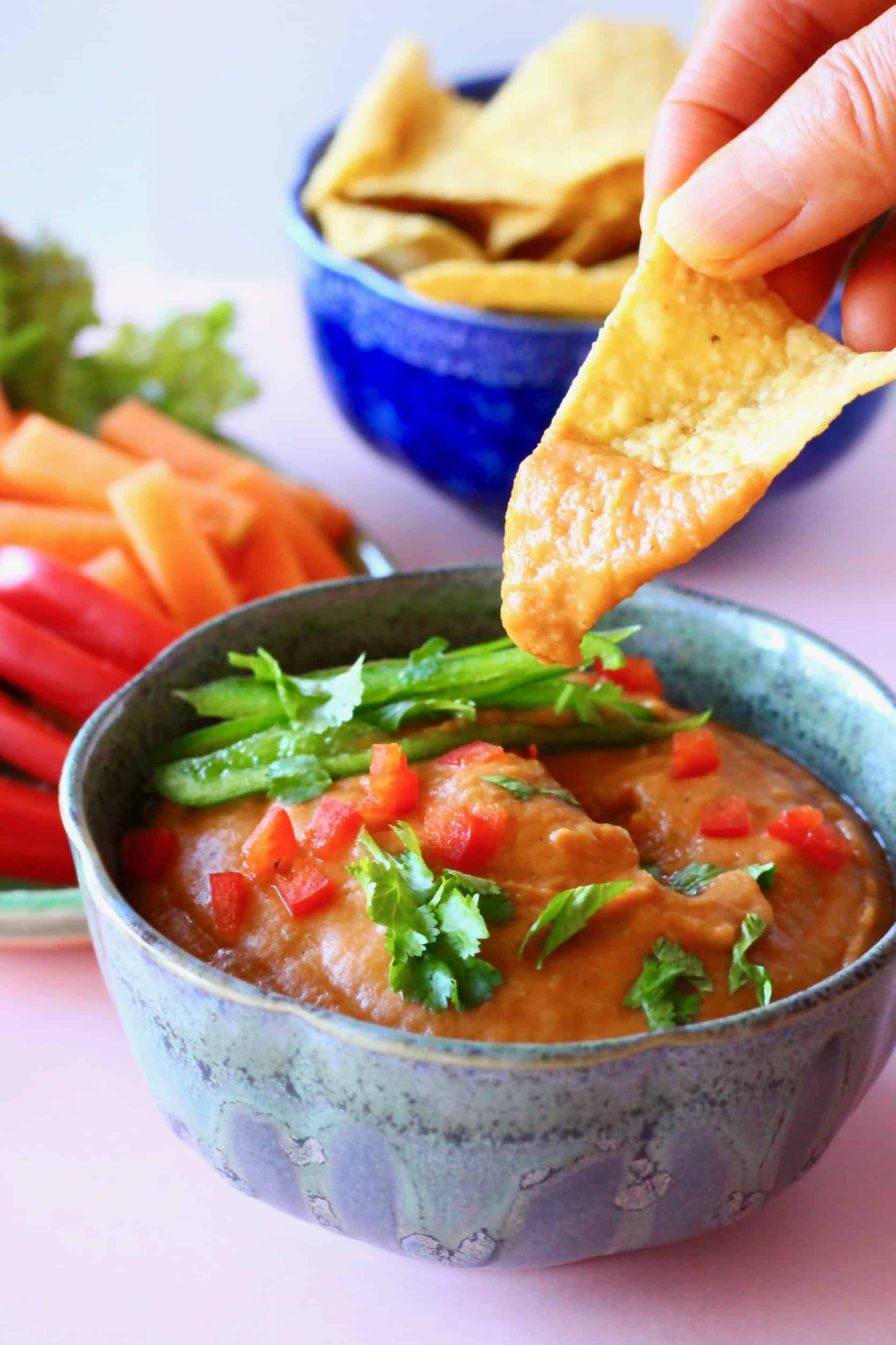A small grey bowl filled with orange queso with a tortilla chip being dipped into it