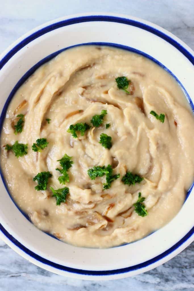 A creamy white dip with caramelised onions in a white bowl with a blue rim against a marble background