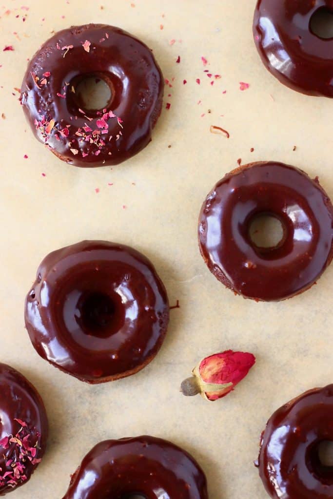 Chocolate glazed mini chocolate donuts on a sheet of brown baking paper decorated with dried roses