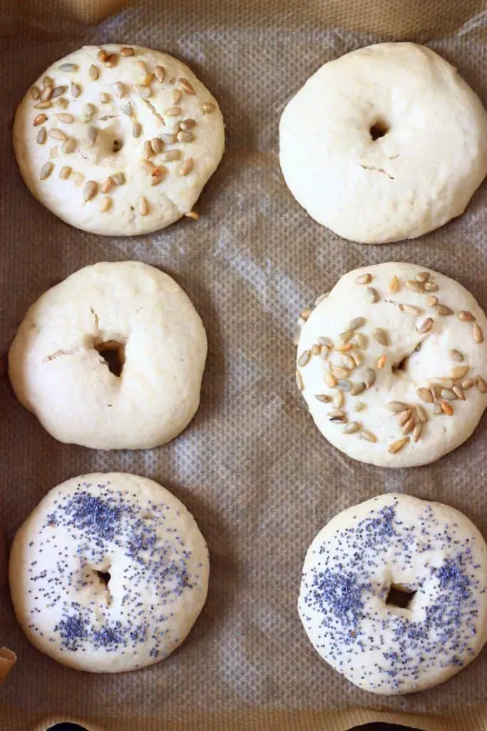 Six bagels topped with seeds on a sheet of brown baking paper
