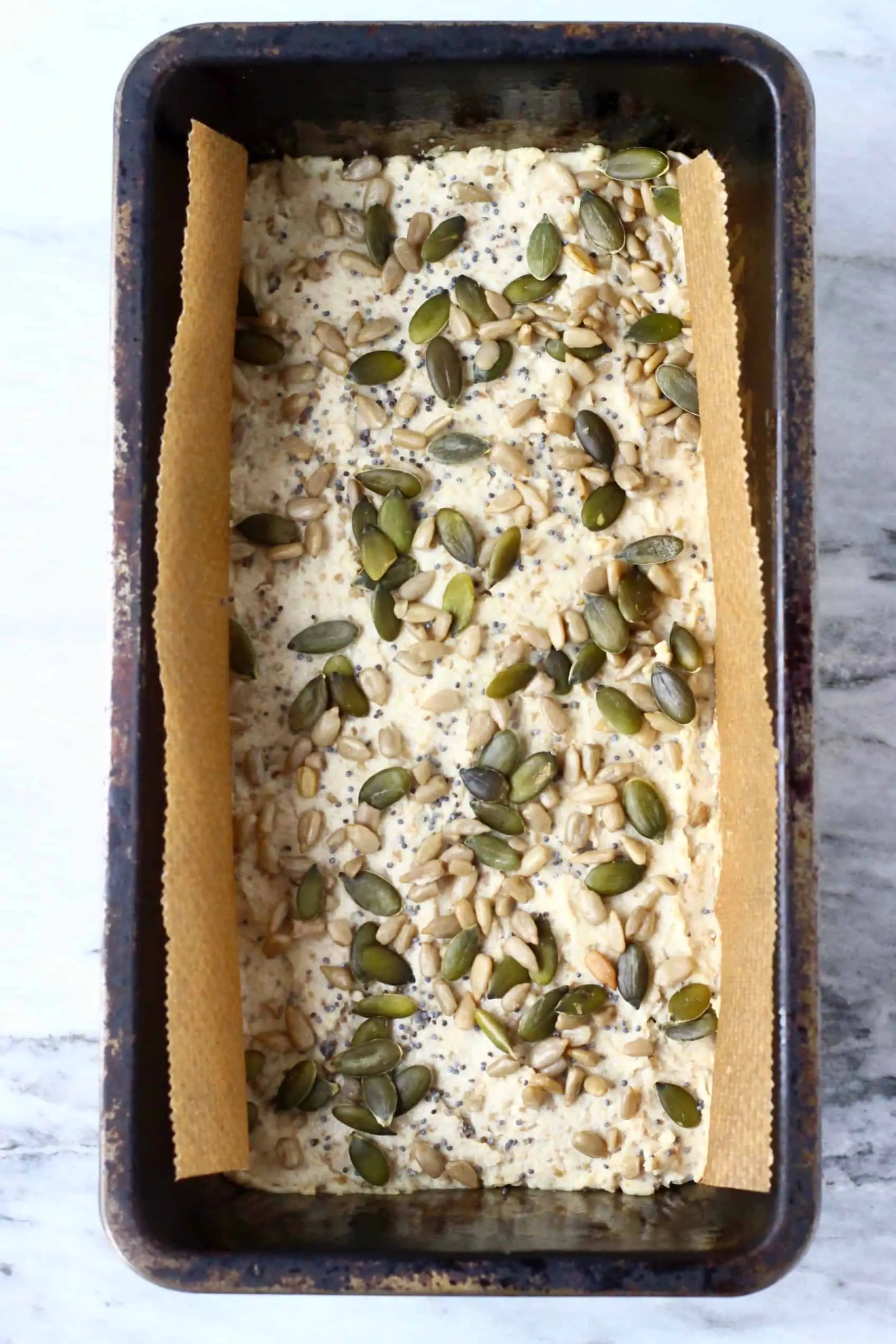 Raw sunflower seed bread batter topped with mixed seeds in a loaf tin lined with baking paper