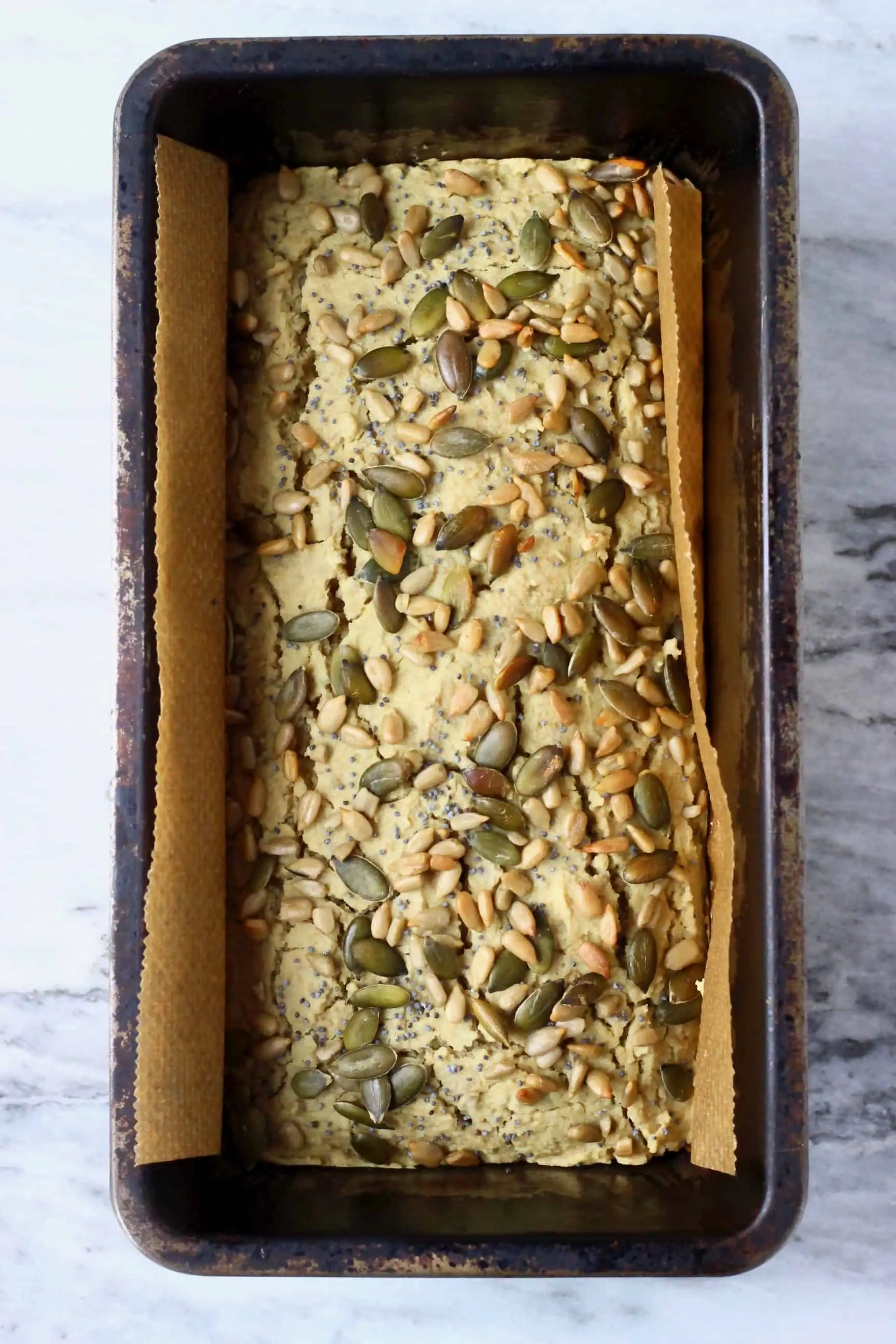 A loaf of sunflower seed bread topped with mixed seeds in a loaf tin